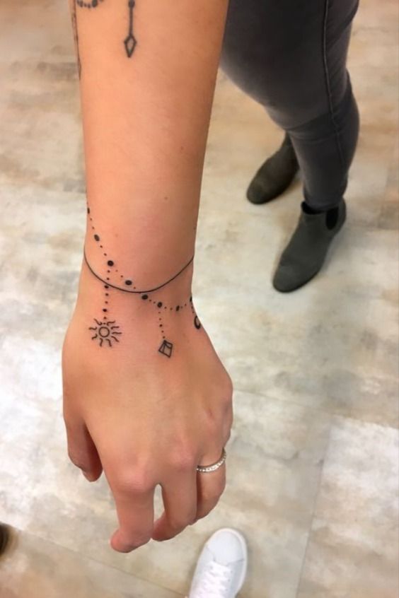 Fine line sun tattoo design for women with a delicate chain on the forearm and hand tattoo ideas