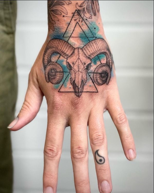 Geometric skull and yin yang tattoo design for men with watercolor accents on hand and finger tattoo ideas